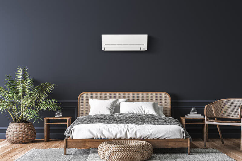 Heat pump on a dark wall above a bed.